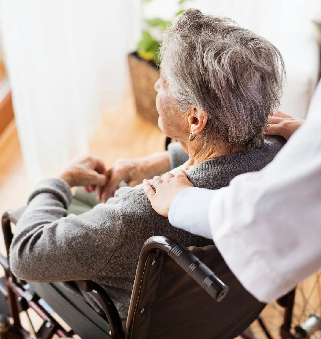 Senior patient in a wheelchair receiving comforting care from a nurse, representing the human impact of nursing home staffing shortages.