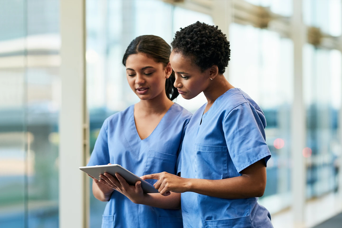 Two nurses from our nursing agency discussing patient care while reviewing information on a digital tablet in a modern healthcare setting.