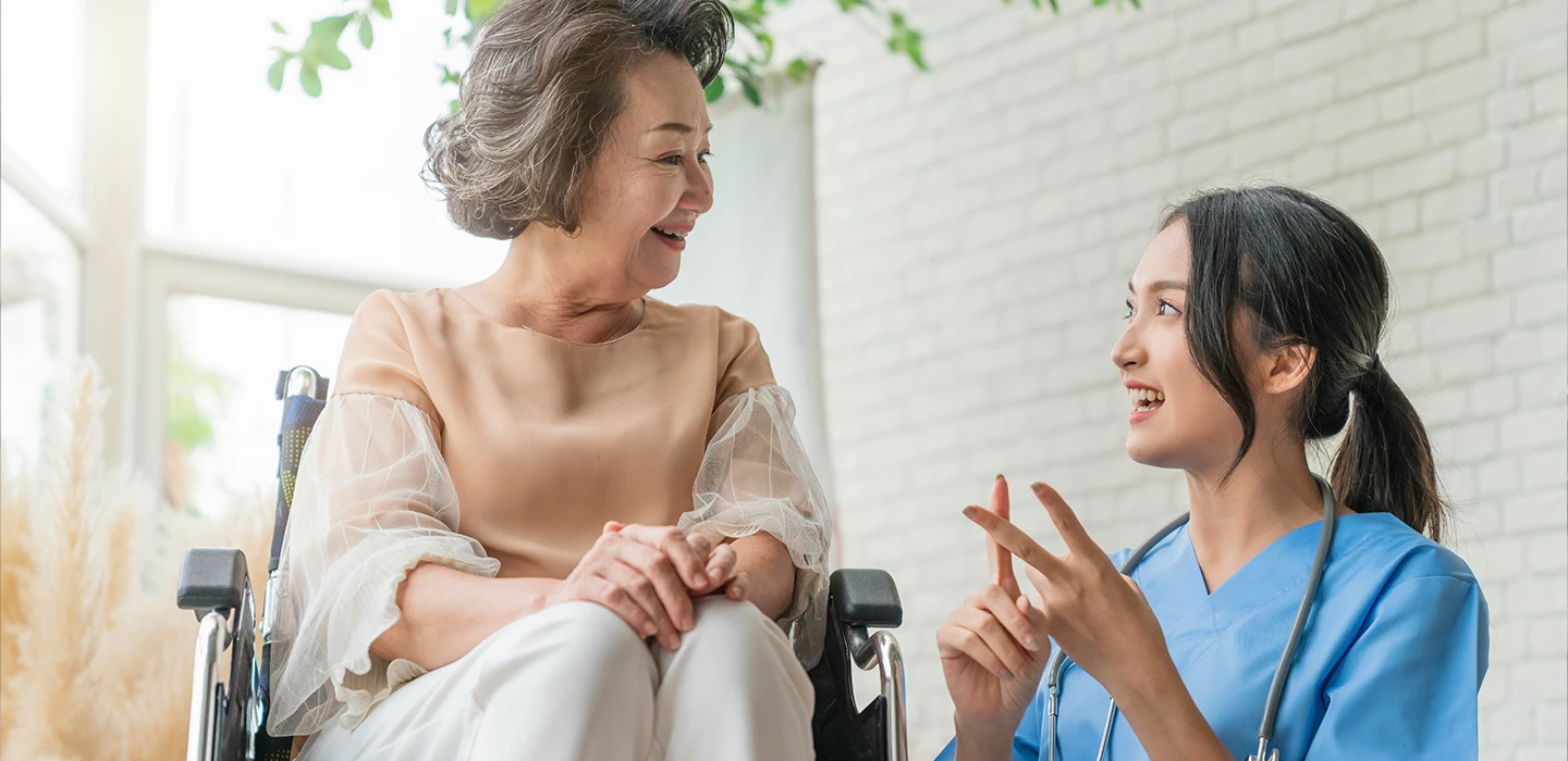 Nurse engaging with a smiling senior in a wheelchair, showing the need for personal connection amidst nursing home staffing shortages.