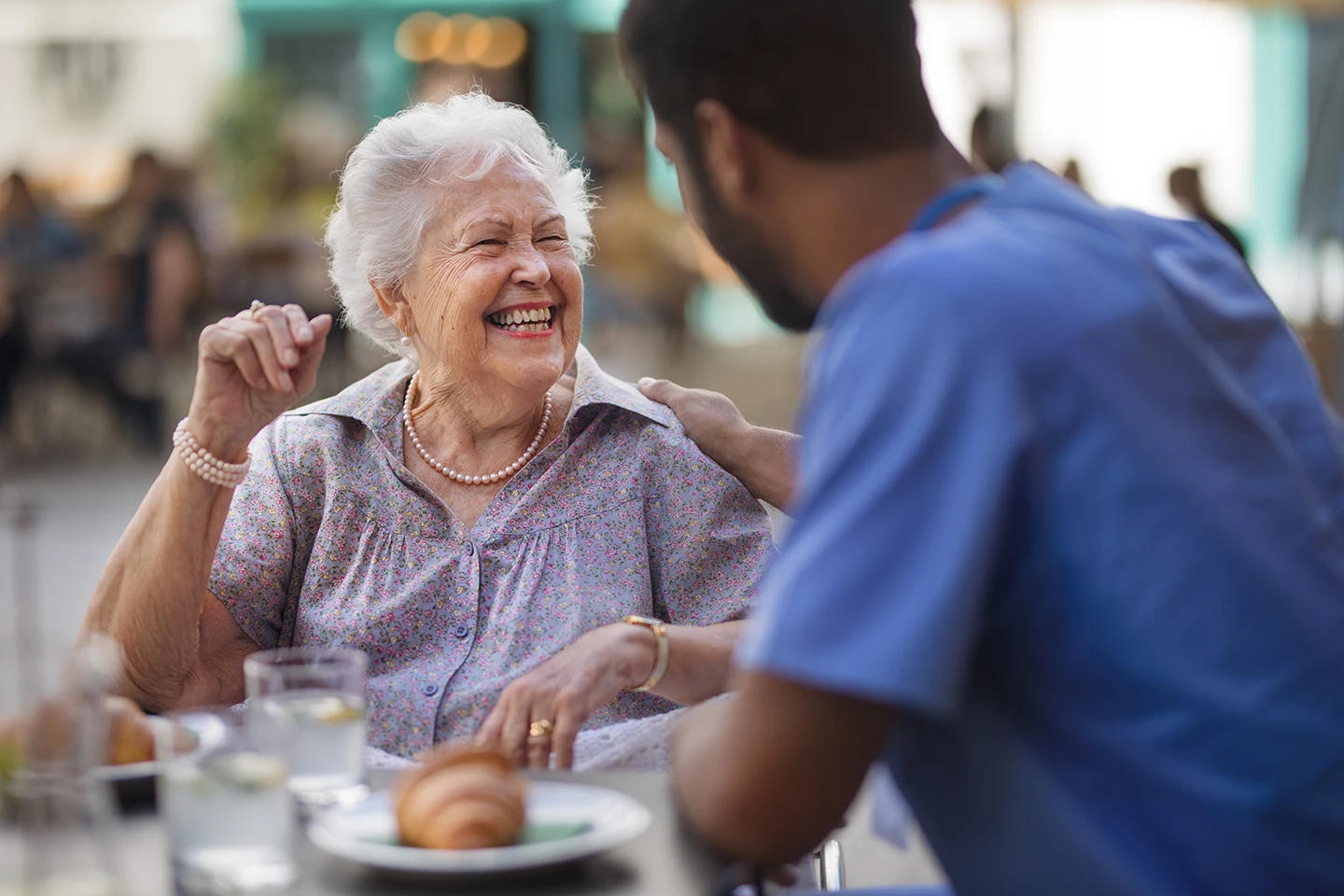 Senior woman enjoying a friendly conversation with a nurse from our agency during an outdoor meal, highlighting personalized senior care.